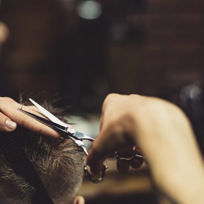 Crop barber doing haircut for client Anonymous stylish barber with tattoos cutting hair of male client in chair.